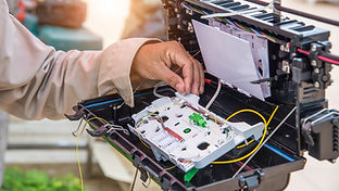 Technician works on fiber optic cables inside black box, sunlight.