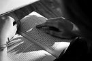 Person's hands holding open book, finger pointing at text, sunlight on pages.