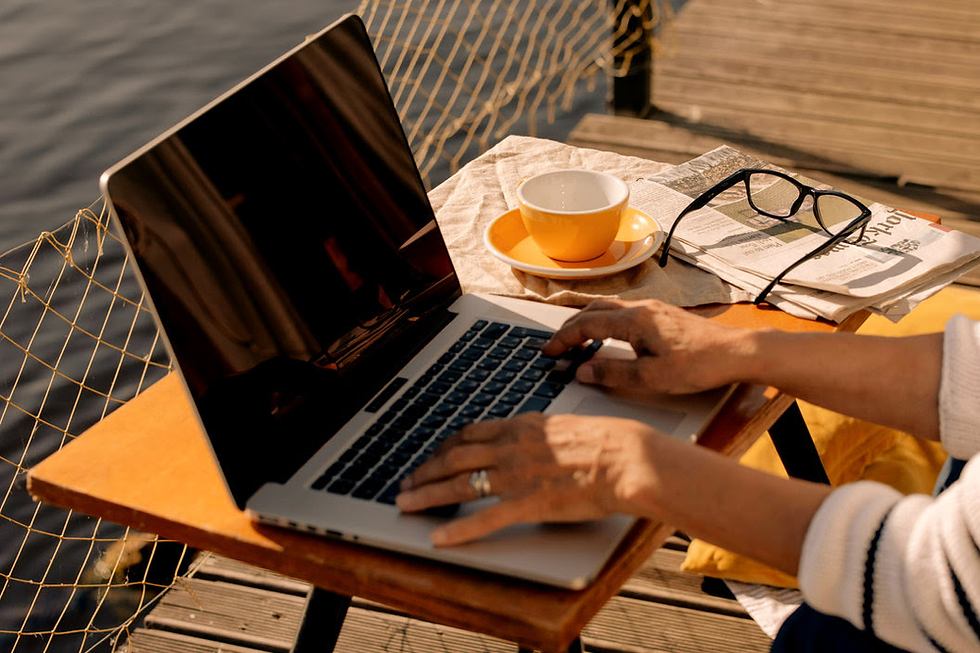 Hands typing on a laptop on a dock by water