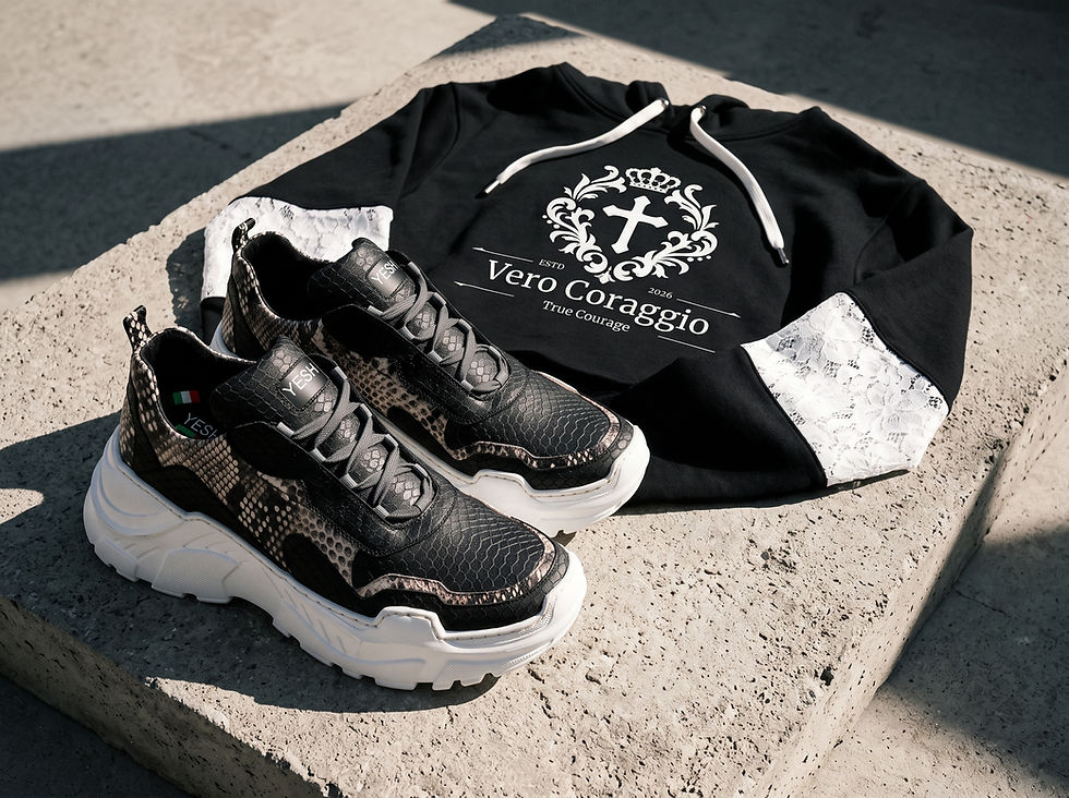 Flat lay of a black cropped hoodie with white lace-panel sleeves and chunky snakeskin-patterned sneakers on a concrete block.