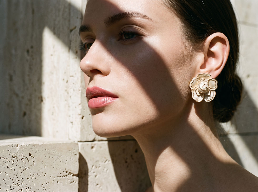 Close-up profile of a woman with floral earrings in warm sunlight, casting shadows against a textured stone wall.