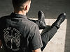 Over-the-shoulder view of a model sitting down wearing black textured leather high-top sneakers and a denim shirt with an angel wings and sword graphic on the back.