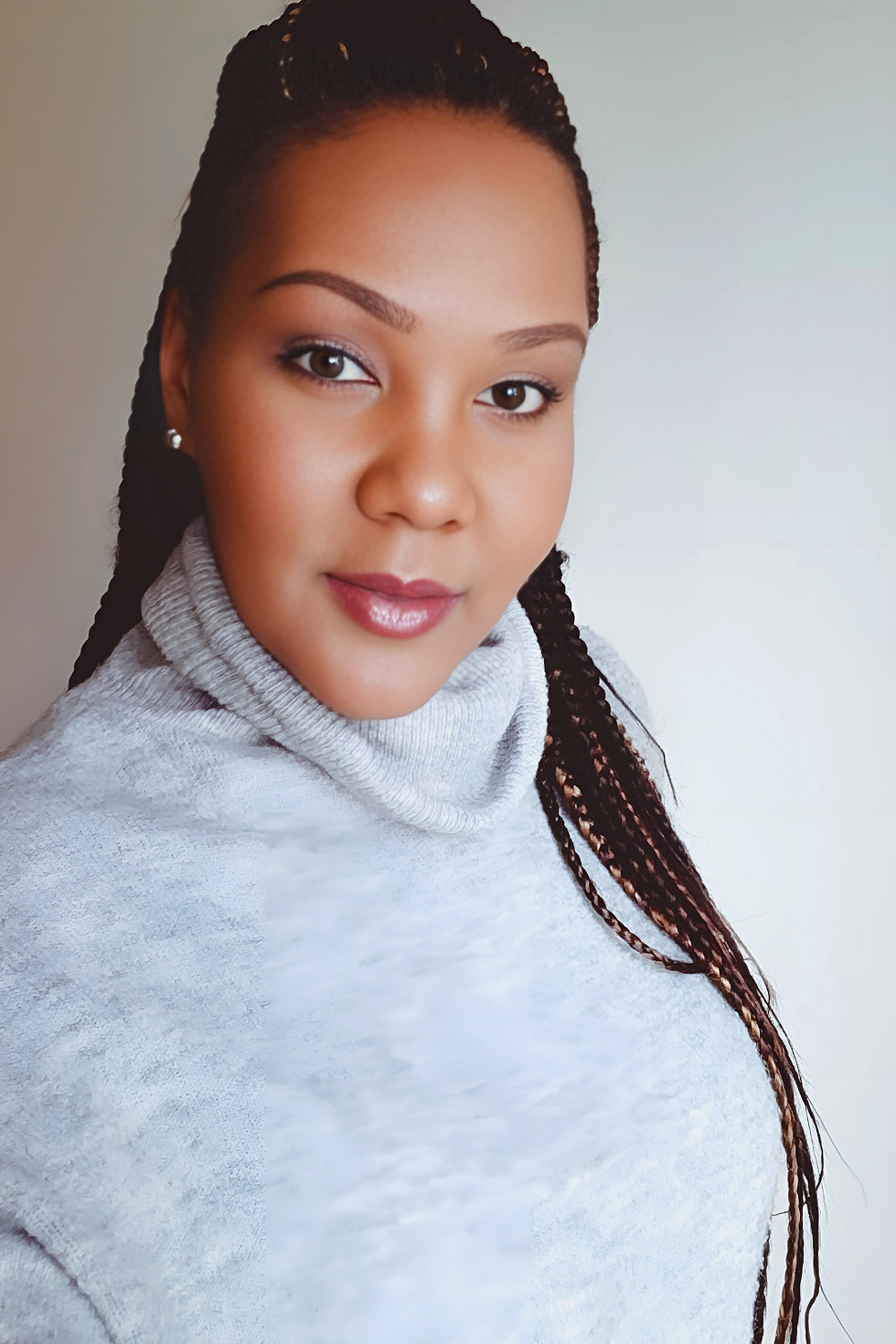 A woman in a light gray turtleneck sweater with braided hair poses against a plain white background, smiling gently at the camera.