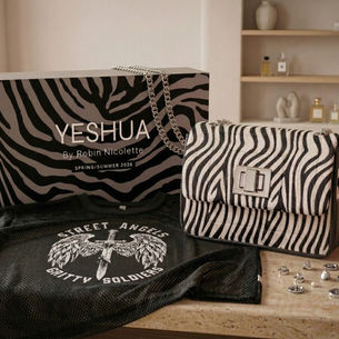 Zebra-patterned bag and box with "YESHUA" text, black mesh shirt with "Street Angels Gritty Soldiers," jewelry on table, cozy room setting.