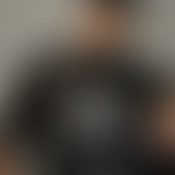 Man in a black mesh shirt with "Street Angels Gritty Soldiers" text, sitting against a gray concrete wall. Tattoos and a calm expression.