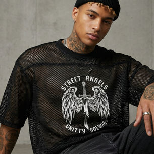 Man in a black mesh shirt with "Street Angels Gritty Soldiers" text, sitting against a gray concrete wall. Tattoos and a calm expression.