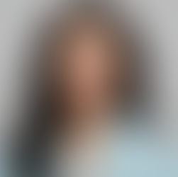 Woman with long dark hair wearing a light blue robe smiles gently against a plain gray background, conveying a calm, serene mood.