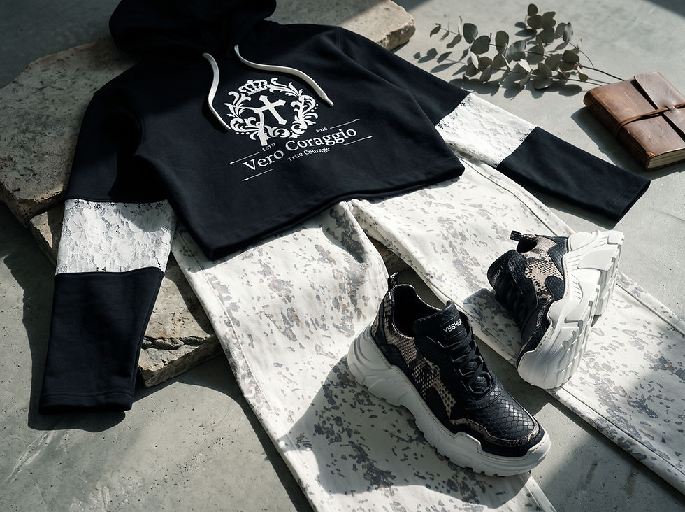 Complete streetwear outfit flat lay including a black lace-sleeve cropped hoodie, off-white patterned jeans, snakeskin sneakers, and a leather journal.