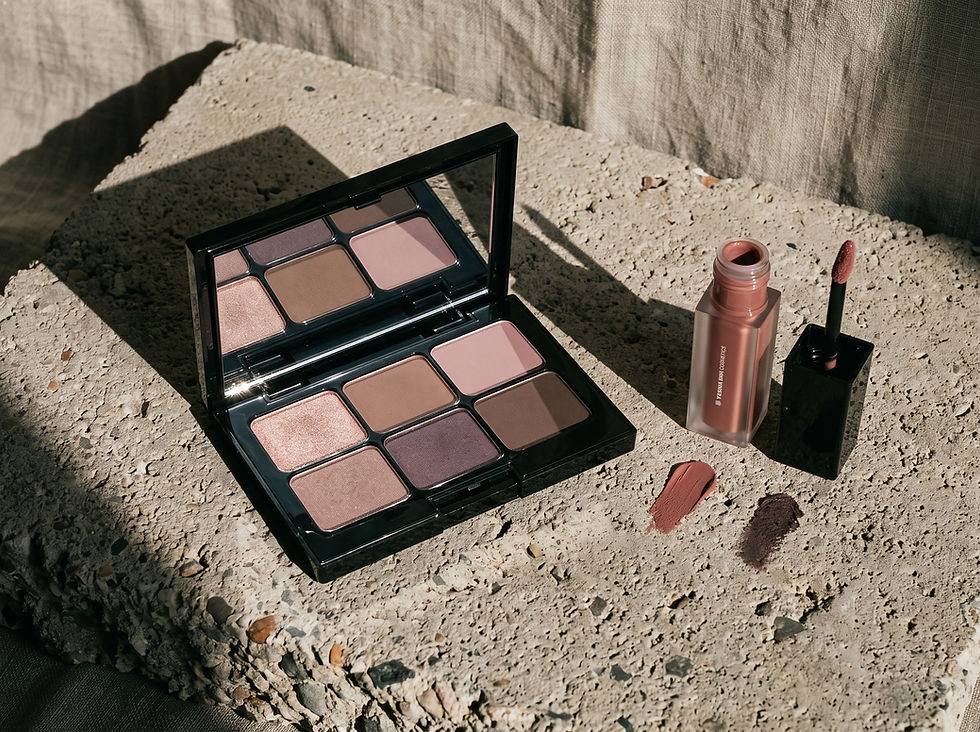 Open eyeshadow palette with lipstick and gloss on sunlit concrete, warm neutral and pink shades, beauty product still life.