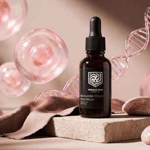 Amber dropper bottle of Yeshua Skin Niacinamide Vitamin Boost Serum beside pink cells and DNA helix on beige stone.