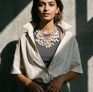 Portrait of a woman in sunlight against a concrete wall, wearing a cream shirt and pearl necklace, with a calm expression