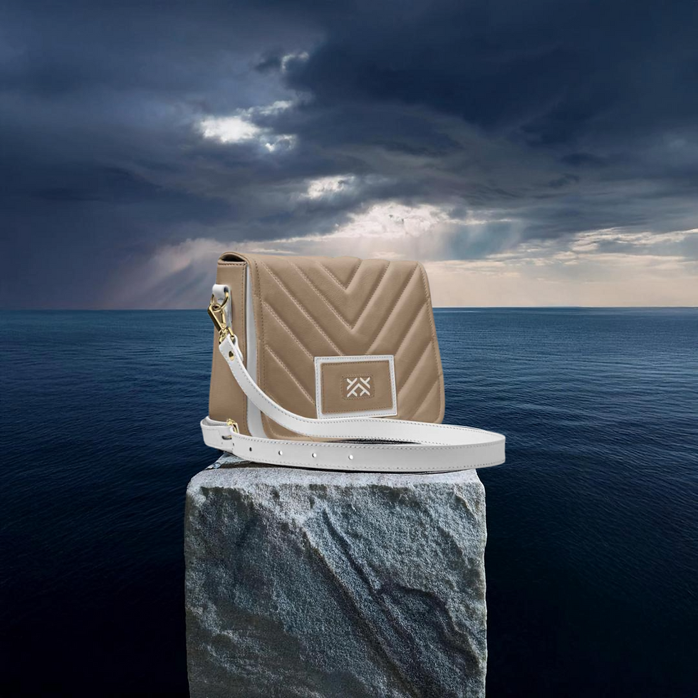A beige quilted bag with white strap sits on a rock by the sea under a dramatic stormy sky, conveying an adventurous mood.