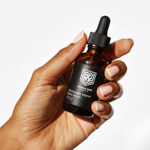 Hand holding a brown dropper bottle labeled "YESHUA SKIN Niacinamide Vitamin Boost Serum" against a white background, neutral mood.