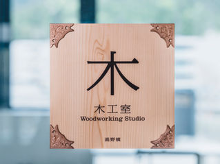 木製の表札。「木工室(Woodworking Studio)」と書かれた杉板に、四隅に装飾金具が取り付けられている。下部に「高野嶺」の名前が刻まれている。