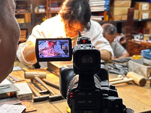 彫金をしている女性職人がテレビカメラで取材されている姿