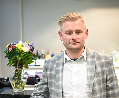Lukasz Wasilewski standing in a suit in front of the reception desk with flowers on display