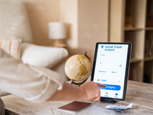 Traveler booking a flight online with passport and travel items on a table.
