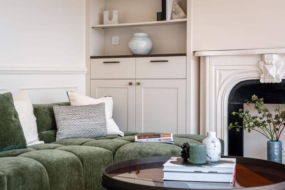 Luxurious modern living room interior designed by MAD Studio featuring a stylish green velvet sofa, elegant throw pillows, a chic round coffee table with decor, and a sophisticated white fireplace. Perfect for contemporary home design and interior decor inspiration by a top interior design firm.