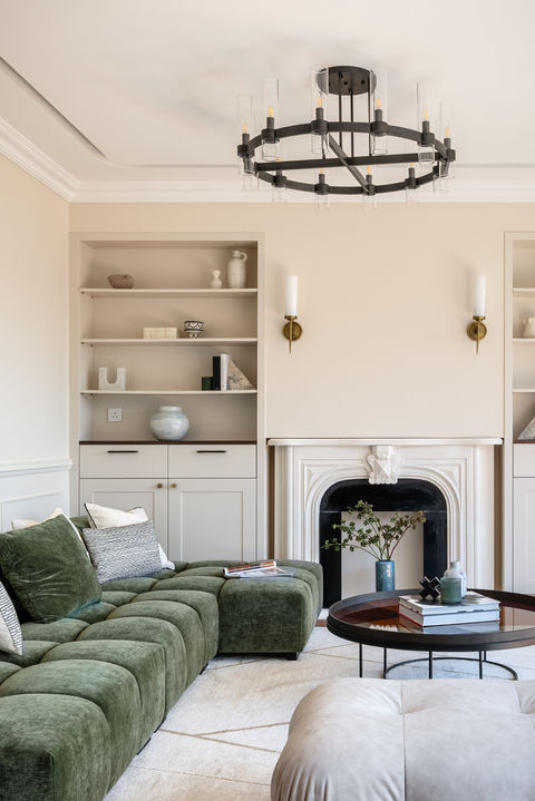 Luxurious living room interior design by MAD Studio featuring a modern green velvet sofa, elegant chandelier, built-in shelves with decorative items, and a stylish fireplace. Perfect for contemporary home decor inspiration.