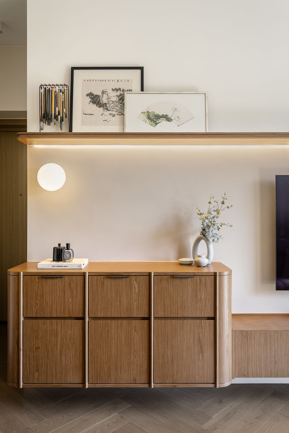 Minimalist wood cabinet with framed art and brushes above, a vase and decor below, and the book EAT DRINK NAP on top.