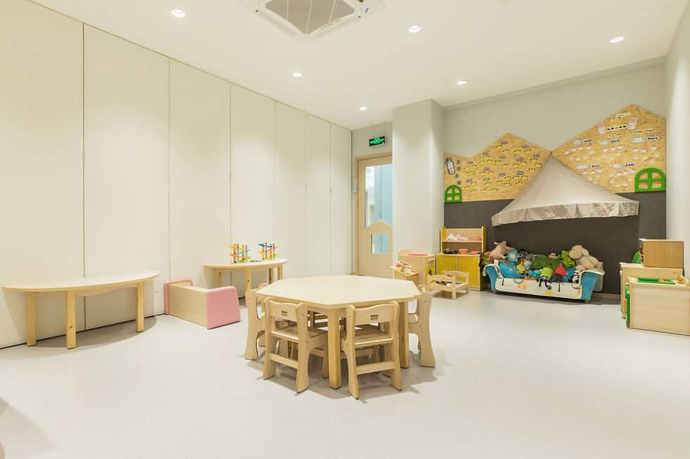 Children's playroom with wooden tables, chairs, toys, and a play tent. Walls have decorative patterns and educational text. Bright, cozy setting.