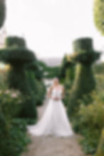 Bride standing in a formal garden during golden hour.