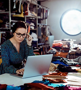 Person working on laptop surrounded by clothes