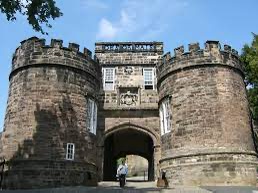 Stone castle entrance with two towers under blue sky, a person is walking here.