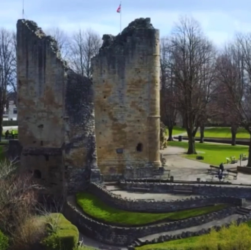 Ruins of an ancient castle with visible text in a lush green park.