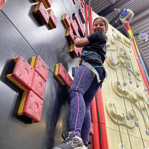 Woman climbing an indoor wall with a smile, wearing safety equipment, Activities in Harrogate.