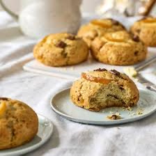 Delicious scones with toppings set on plates, butter knife, and white linen.