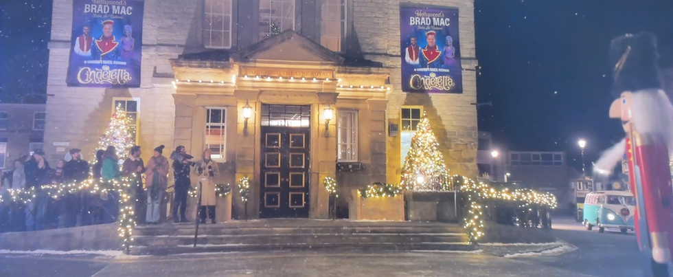Entrance of building with illuminated lights and Brad Mac poster, festive scene outside.