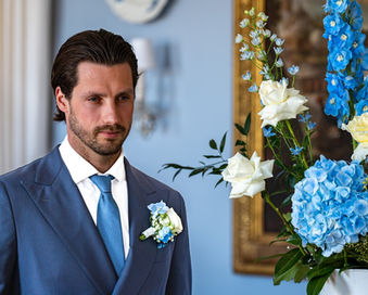 Bräutigam im blauen Anzug vor Blumenarrangement