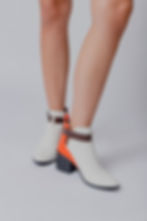 Black chunky heel ankle boot, with opaque white color on the front and carrot orange trim on the back.