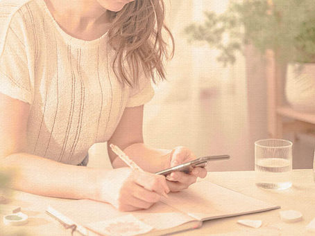 Woman writing in a notebook while checking her phone at a table, illustrating the mental load of planning and household responsibilities