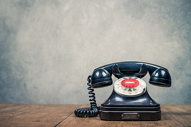 Retro old black rotary telephone on table front textured concrete wall background. Vintage