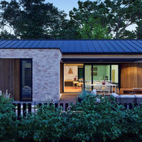 Side view of a small modern 4-bedroom one story house plan, featuring evening architectural lights