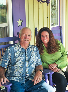 Paul & Holly Simonette (co-owners) sitting on their front porch showing green walls and purple shutters on their house.