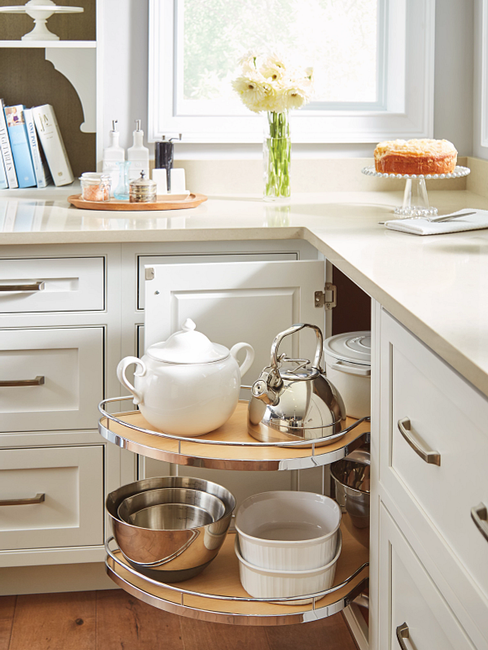 A lazy Susan cabinet for a kitchen with tea kettles and bowls.