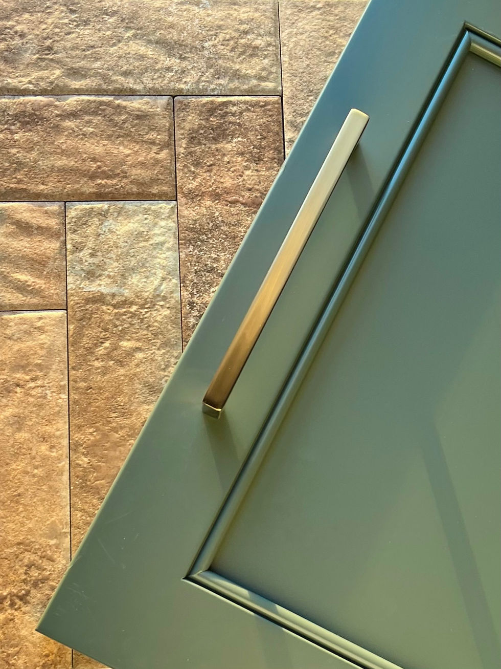A green cabinet door with stone backsplash and a brass handle.