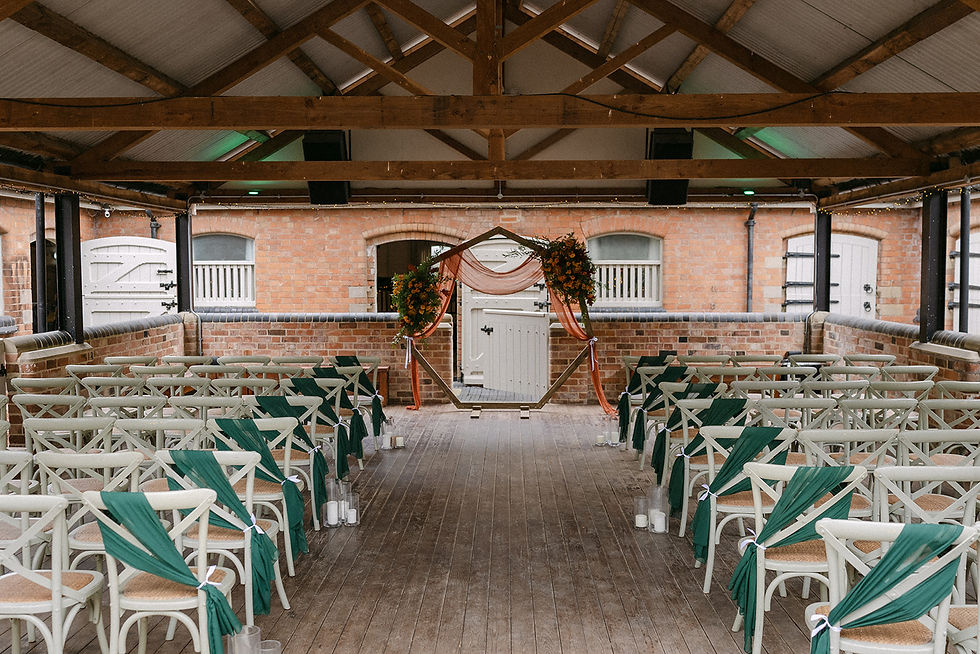Rustic wedding ceremony setup in a brick venue with draped chairs, a floral arch, and candles. Warm, intimate atmosphere.