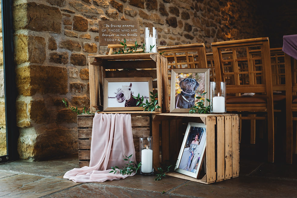 Wooden crates with framed photos, candles, and greenery in a stone-walled room. Text reads "In loving memory of those...".
