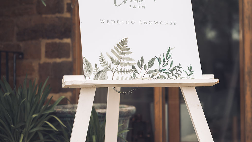 White easel sign reads Welcome to the Crockwell Farm Wedding Showcase, with leafy floral border outside a rustic doorway.