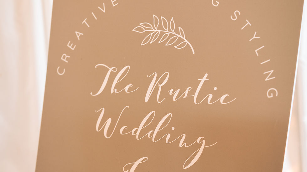 Wedding sign on an easel reads Creative Wedding Styling, The Rustic Wedding Co., Est. 2014, against white drapes.
