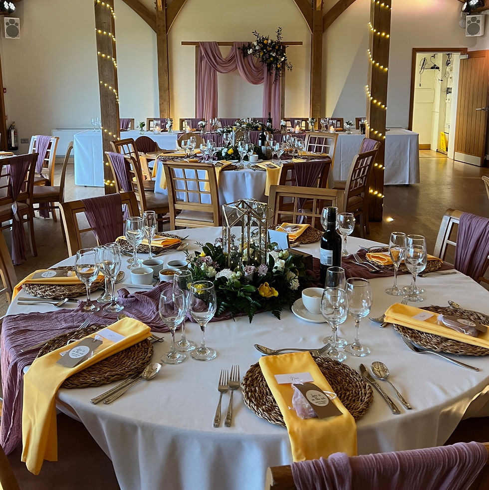 Elegant banquet setup with round tables adorned with yellow and purple accents, flower centerpieces, and wine. Soft lighting adds warmth.