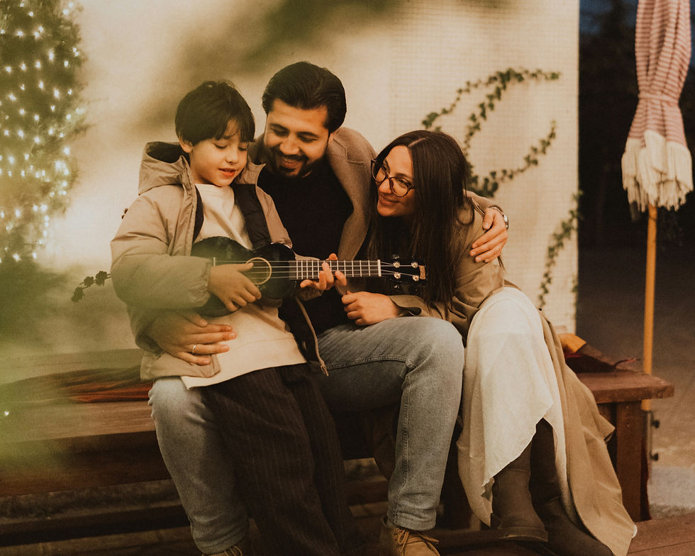 A family sits on a bench, the child holds a ukulele with parents embracing. Warm lighting, festive atmosphere, and soft-focus background.