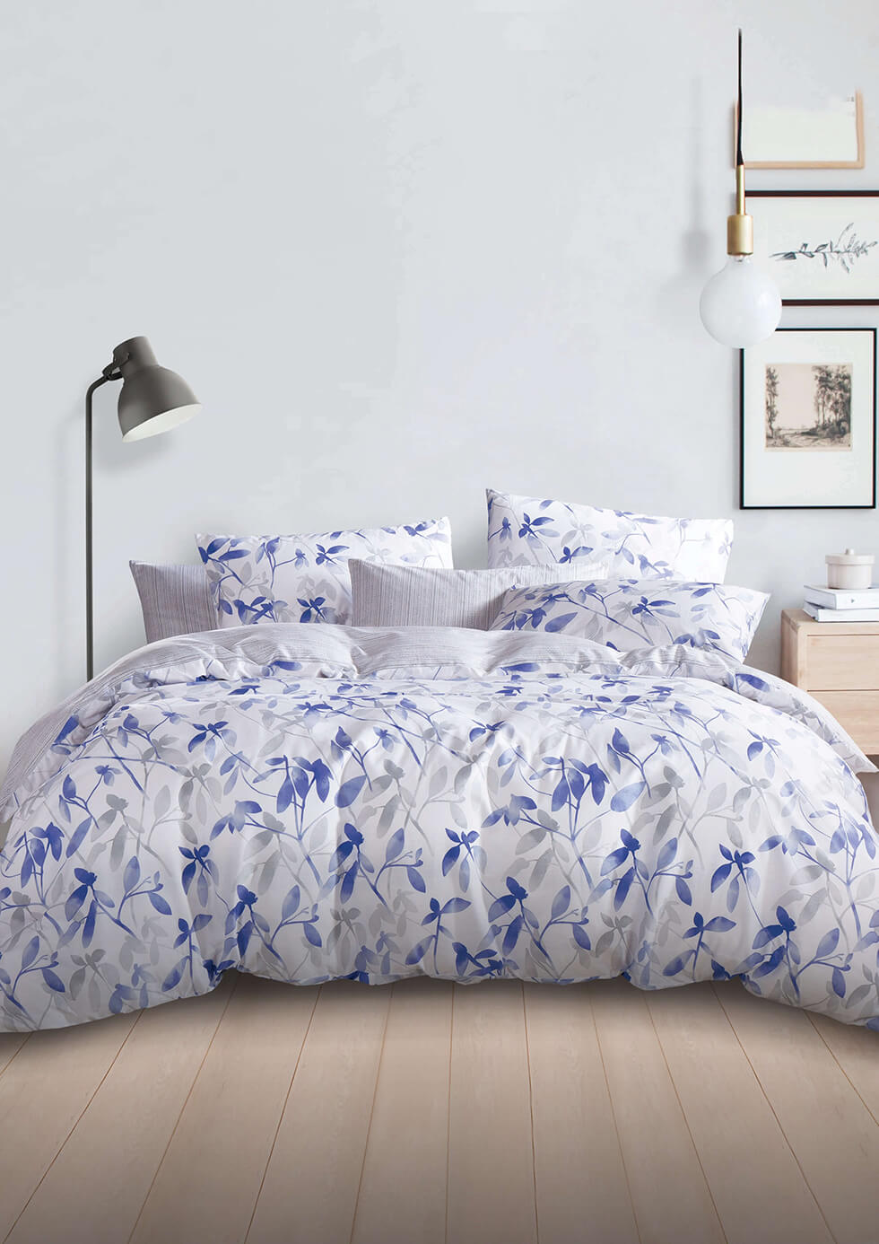 Hooga blue floral pattern bed in a minimalistic room with standing lamp on the left and some picture frame on the right side of the wall