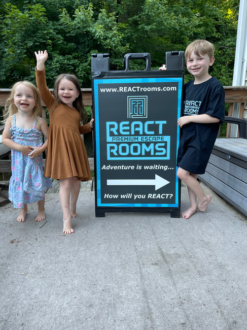 Three children standing beside a REACT Premium Escape Rooms sign outdoors, showing the growth of the business from its early days to today.