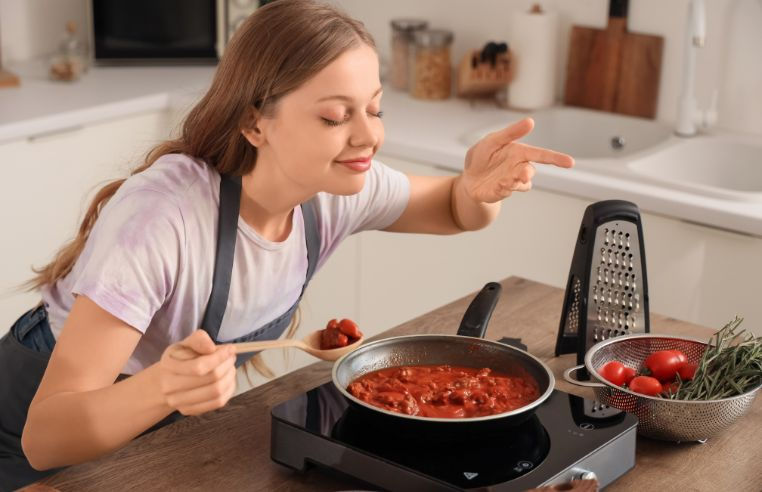 Woman leaning over a pan of tomato sauce, smelling food cooking as part of the cephalic phase of digestion