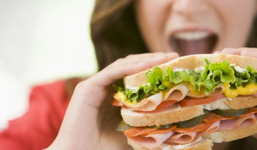 Woman about to bite into a large sandwich, illustrating how digestion begins before food enters the mouth
